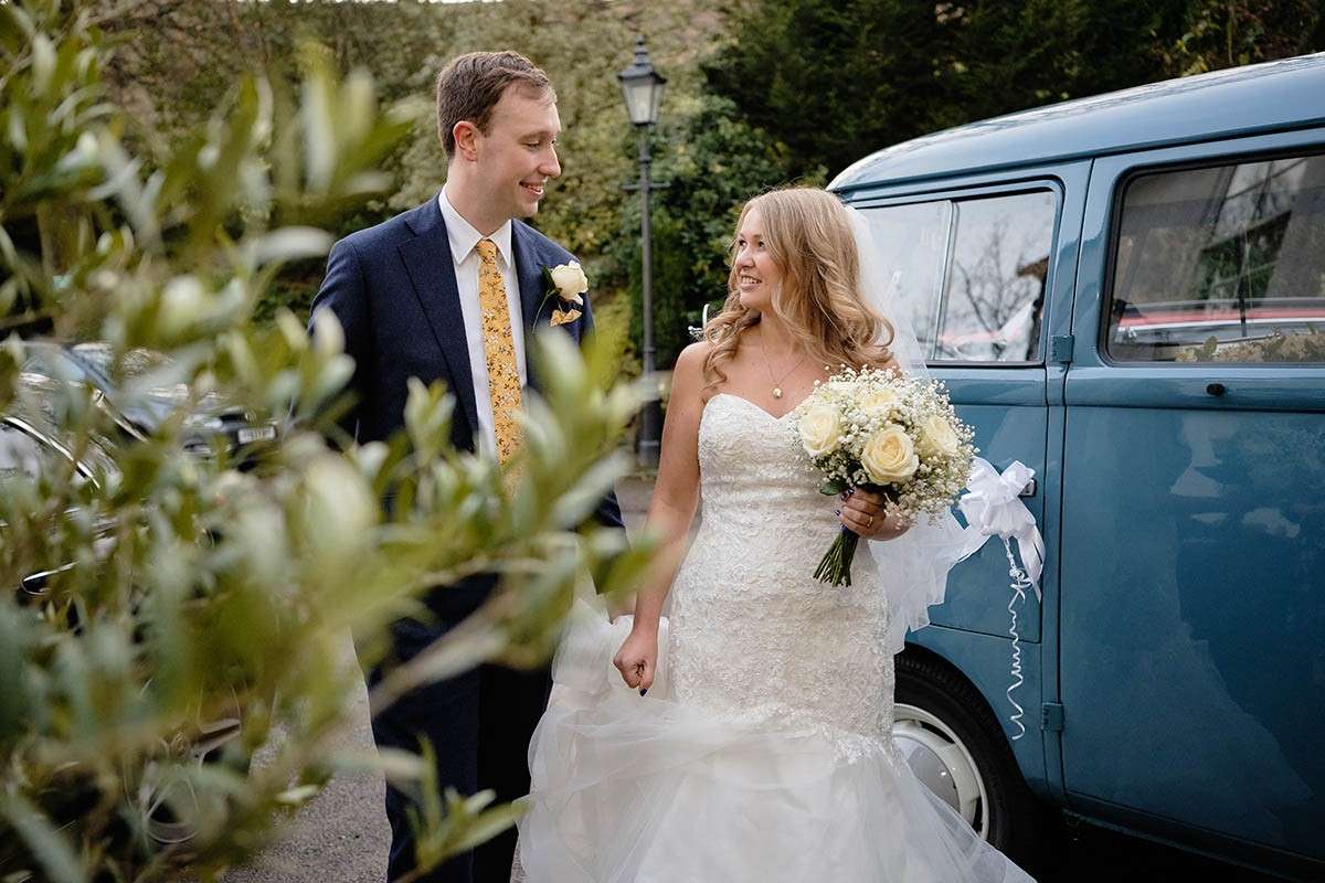 Happy wedding photography: bride and groom grin happily at each other by a blue VW Camper van after their Derbyshire wedding.